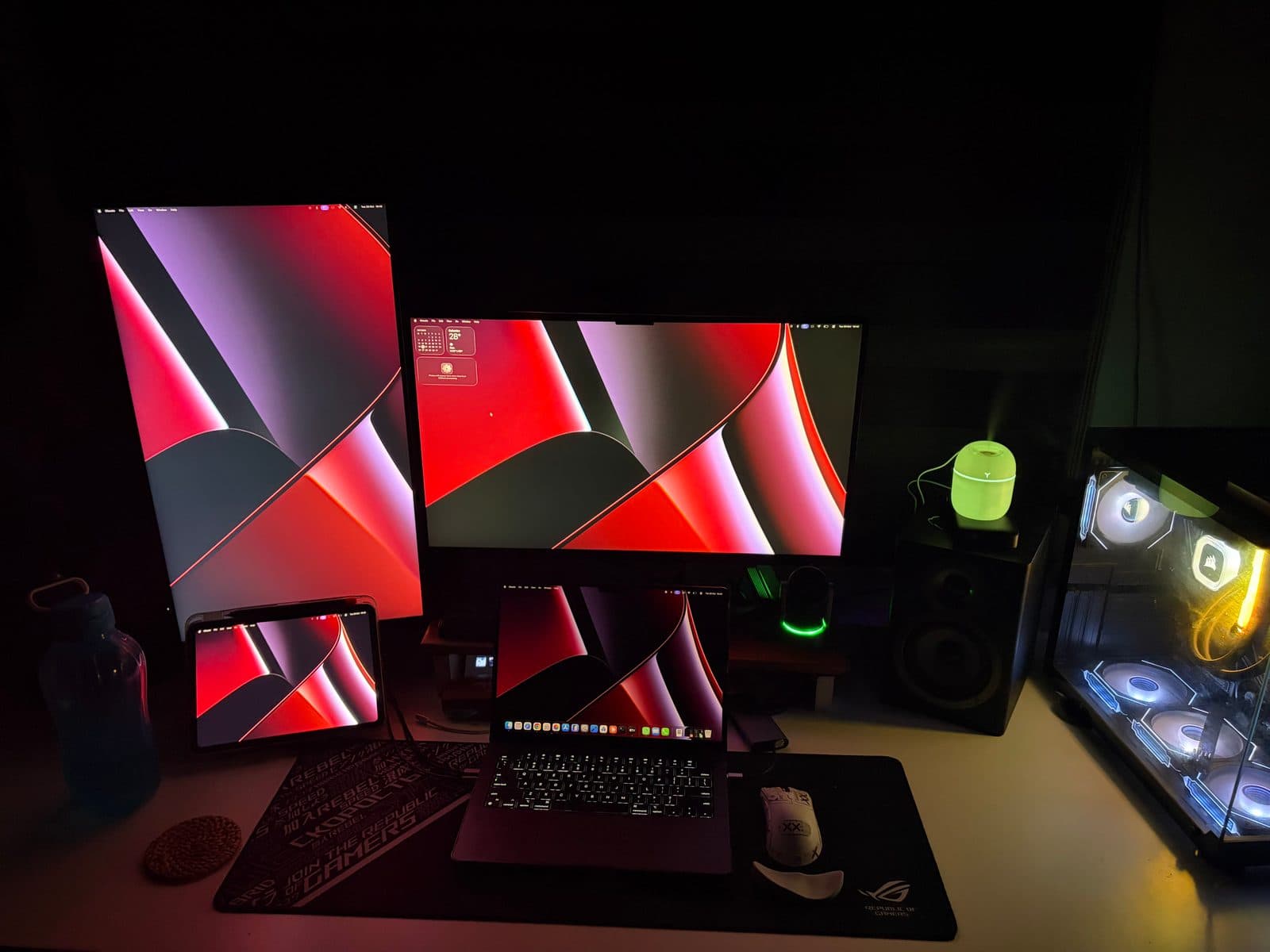 Dark desk setup with three screens, a laptop and a glowing green Colorful Egg Humidifier beside a speaker