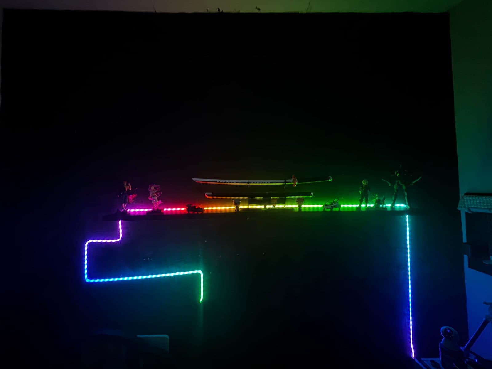 Colourful RGB neon strip running along a wall and a shelf lighting an anime figure and sword collection