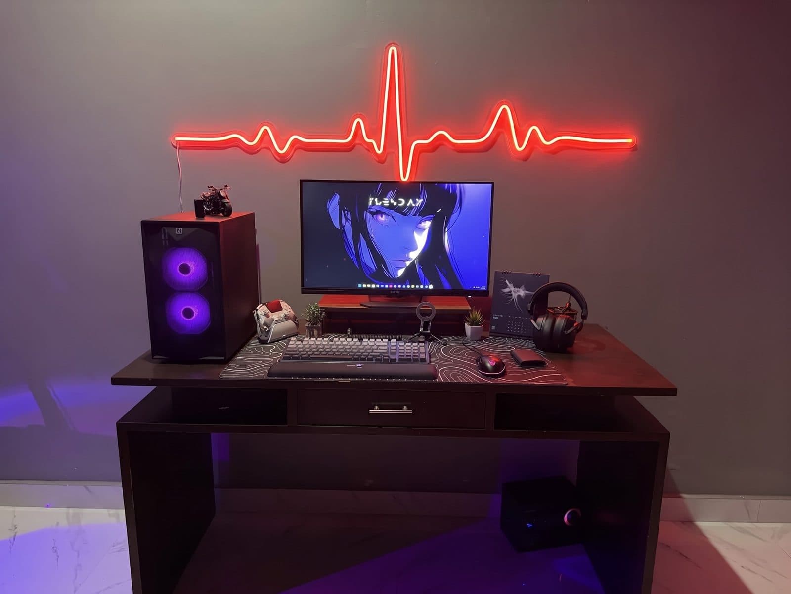 Red neon strip shaped into a heartbeat line on a wall above a desk with a monitor, PC and headphones